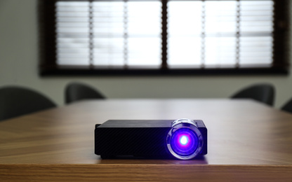 Photo of Modern video projector on wooden table in conference room