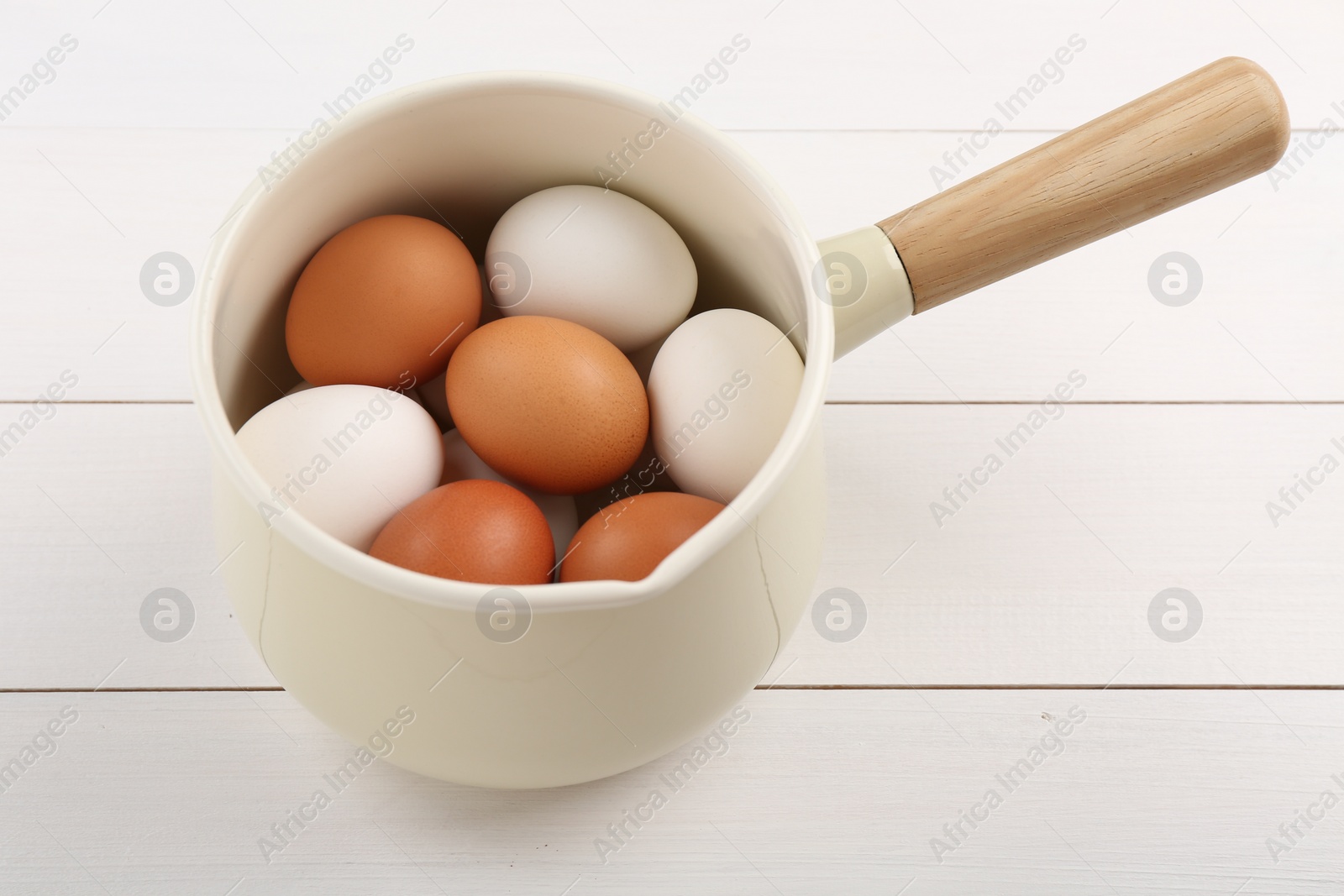 Photo of Unpeeled boiled eggs in pan on white wooden table, closeup
