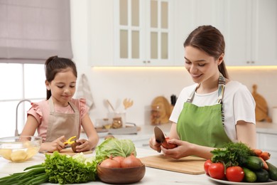 Photo of Mother and daughter peeling vegetables at table in kitchen