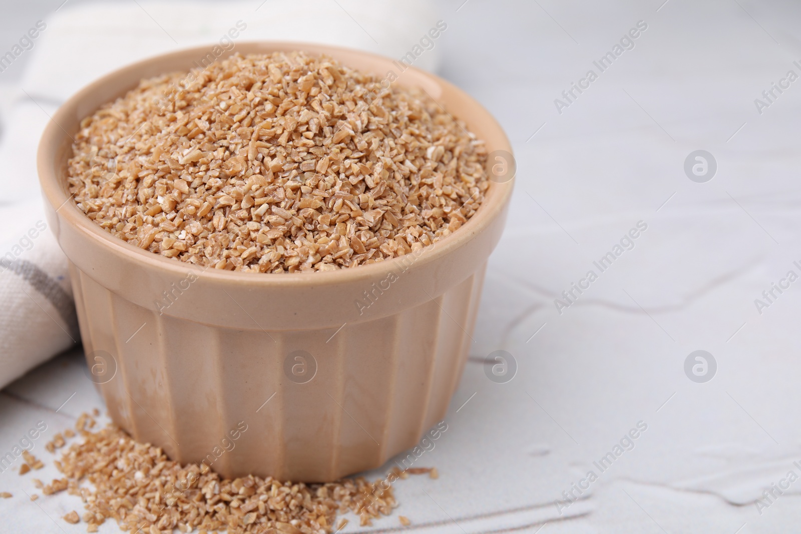Photo of Dry wheat groats in bowl on white textured table, closeup. Space for text