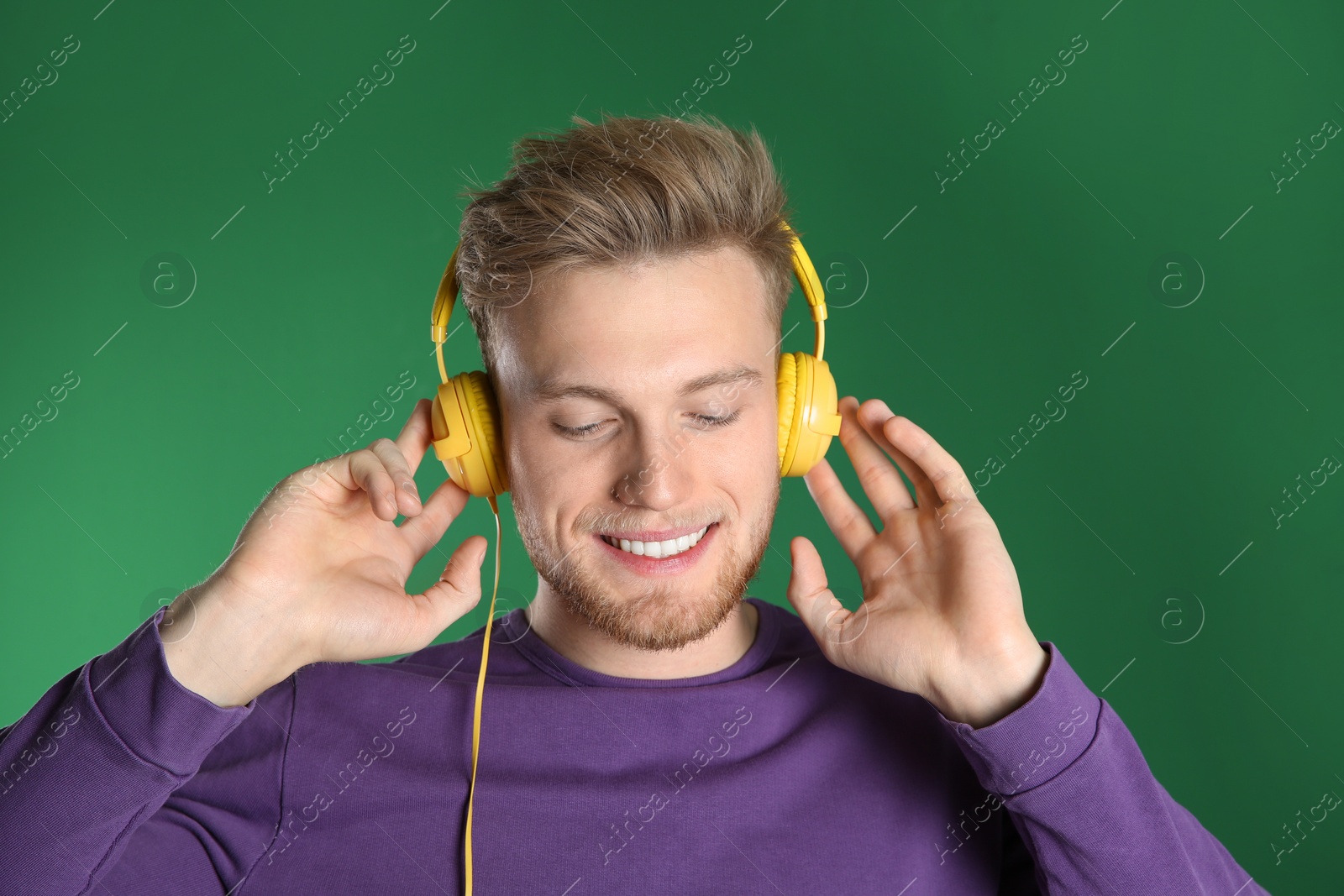 Photo of Handsome young man listening to music with headphones on color background