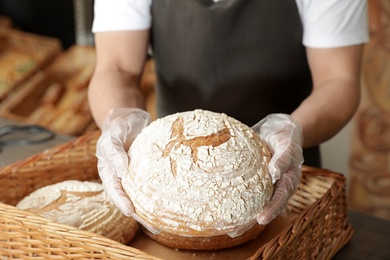 Photo of Professional baker holding loaf of bread over tray in store, closeup