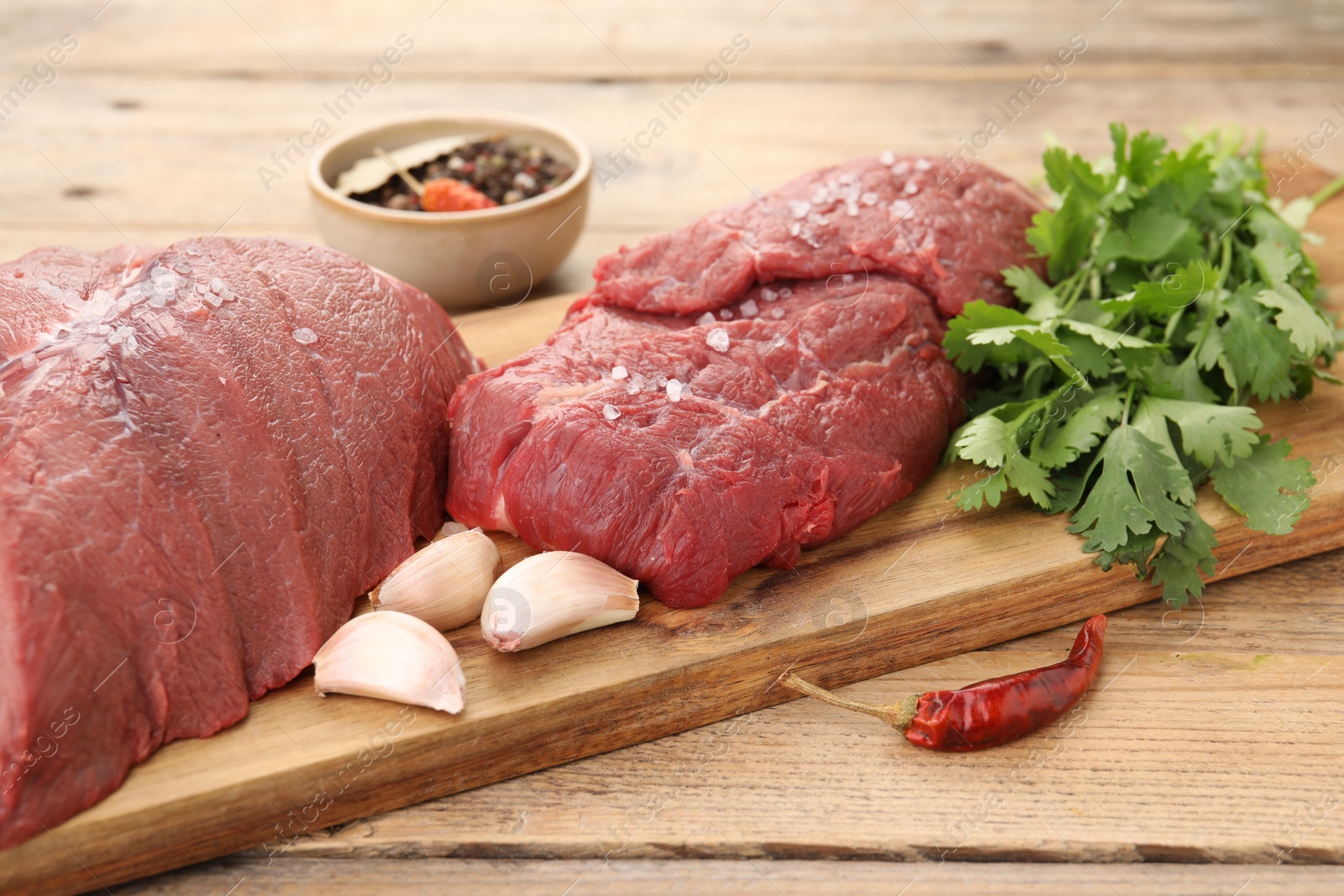 Photo of Pieces of raw beef meat, parsley, garlic and spices on wooden table, closeup