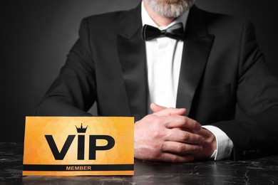 Photo of Man sitting at table with VIP sign on black background, closeup