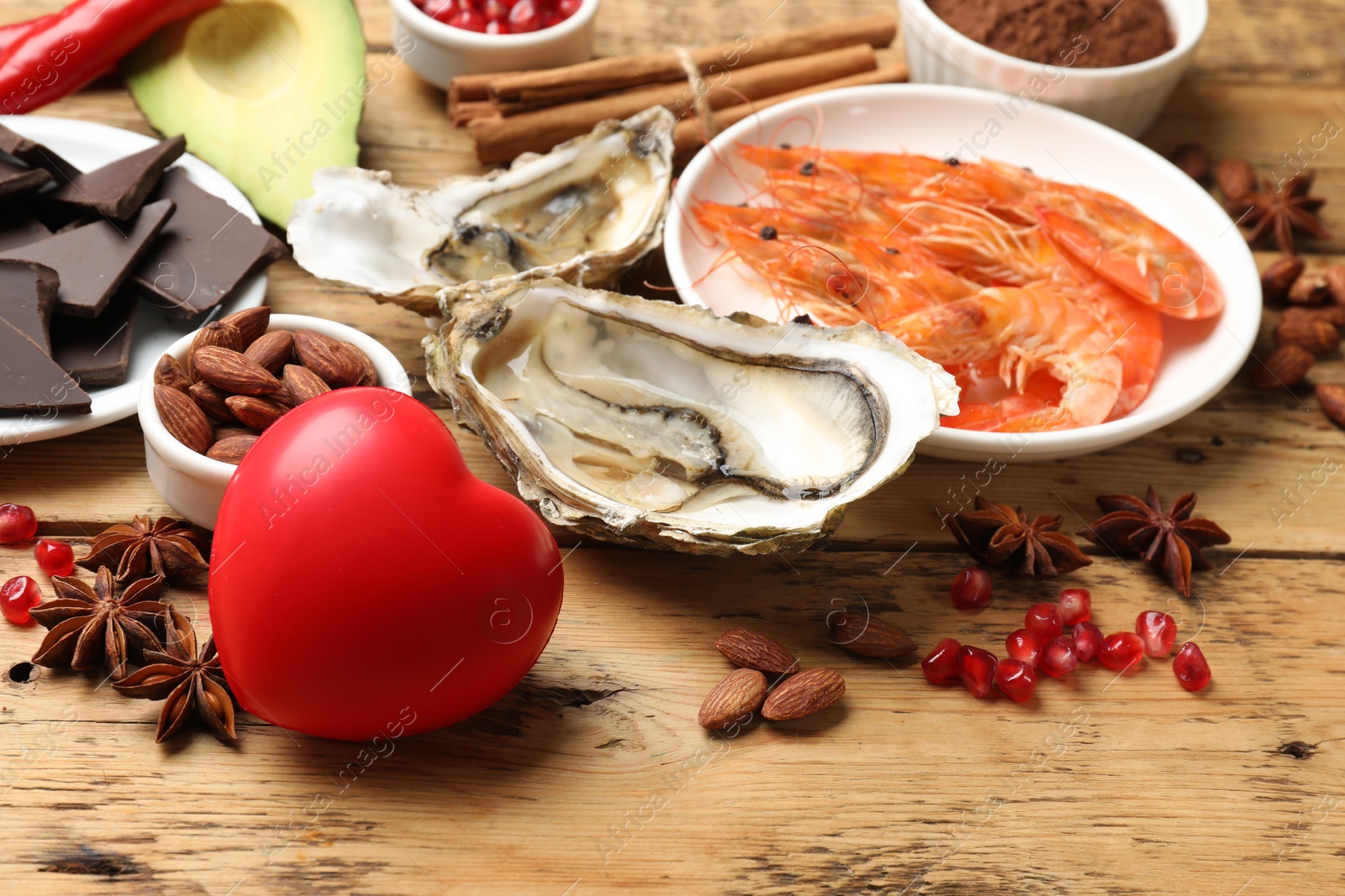 Photo of Natural aphrodisiac. Different food products and heart model on wooden table, closeup