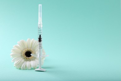 Photo of Cosmetology. Medical syringe and gerbera flower on turquoise background, space for text