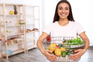 Photo of Young woman with shopping basket full of products in grocery store