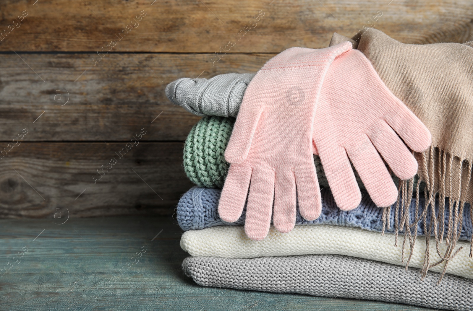 Photo of Stacked sweaters and gloves on blue table, closeup with space for text. Autumn clothes