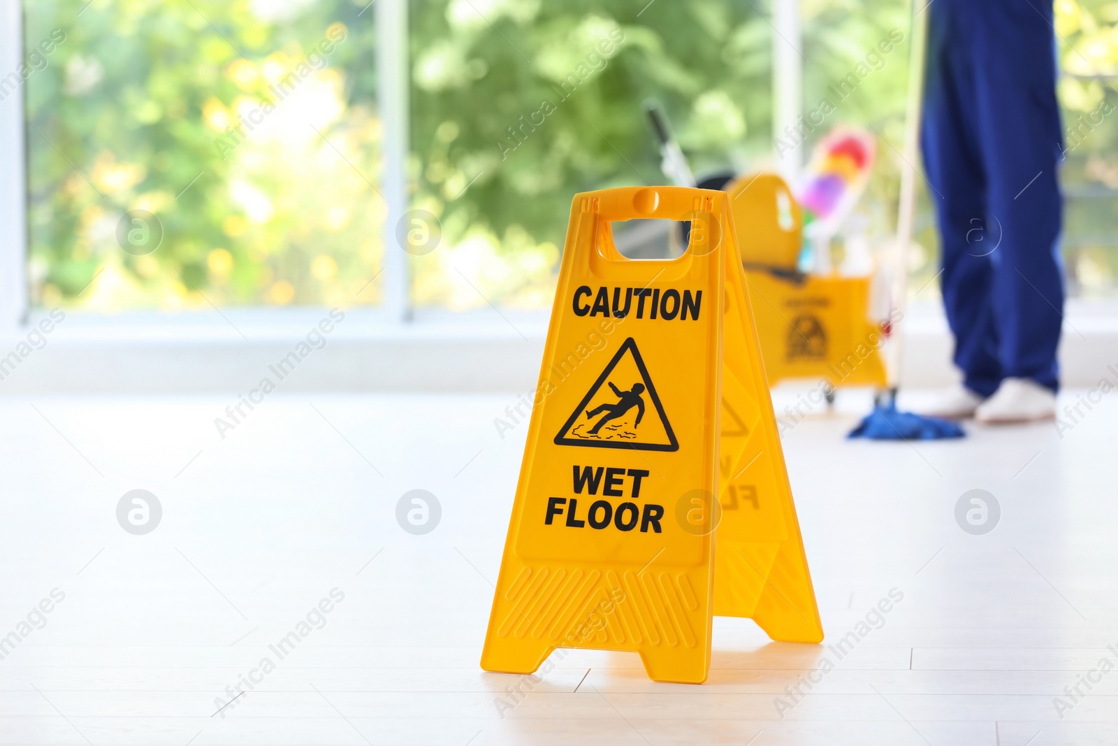 Photo of Safety sign with phrase Caution wet floor and blurred cleaner on background