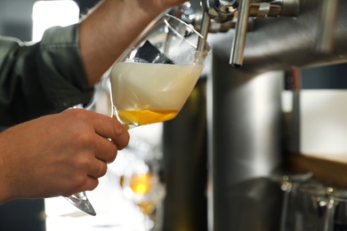 Bartender pouring fresh beer into glass in pub, closeup