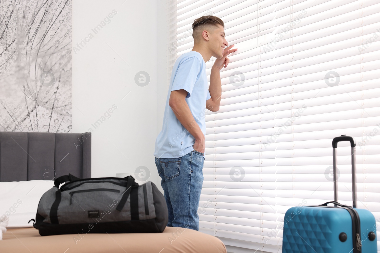 Photo of Smiling guest looking through blinds in stylish hotel room