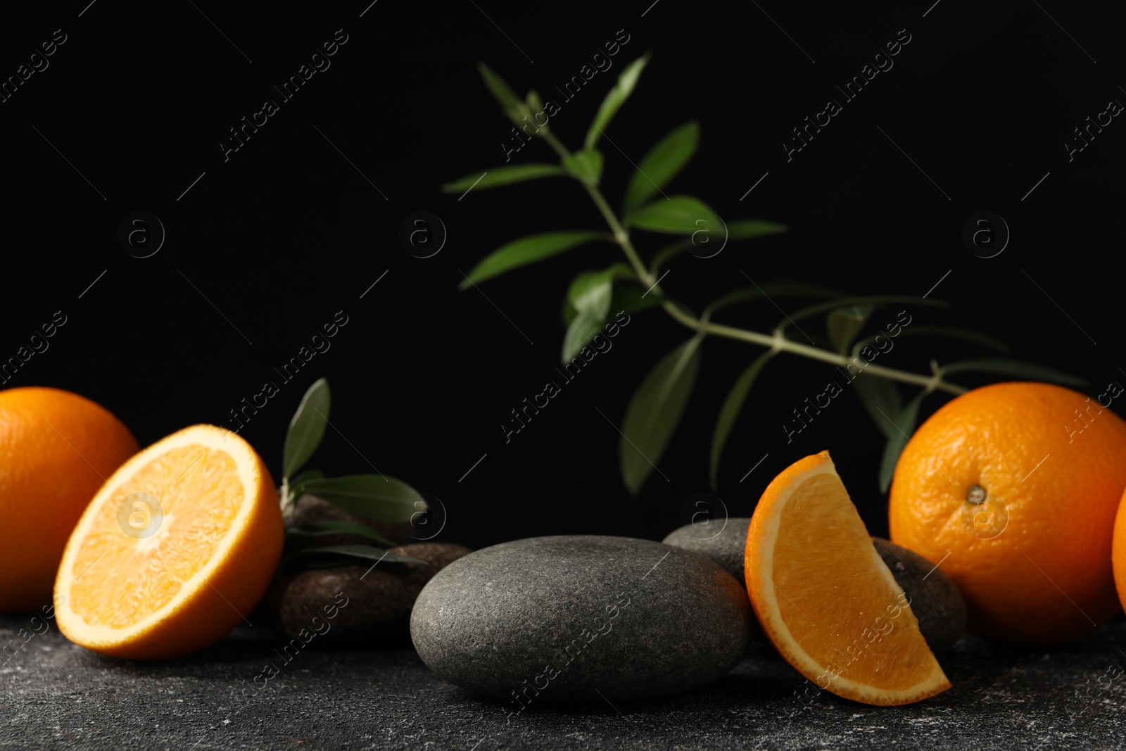 Photo of Tasty fresh oranges, stones and leaves on black table, closeup