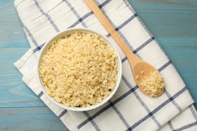 Delicious bulgur in bowl and spoon on light blue wooden table, top view