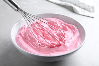 Photo of Whipping pink cream with balloon whisk on light grey table, closeup