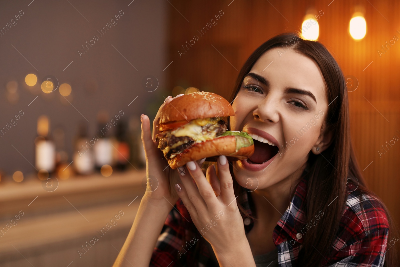 Photo of Young woman eating tasty burger in cafe