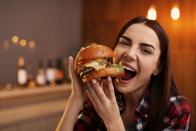 Young woman eating tasty burger in cafe