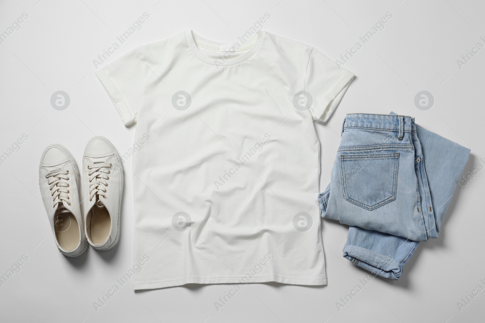 Photo of Stylish t-shirt, jeans and sneakers on white background, flat lay