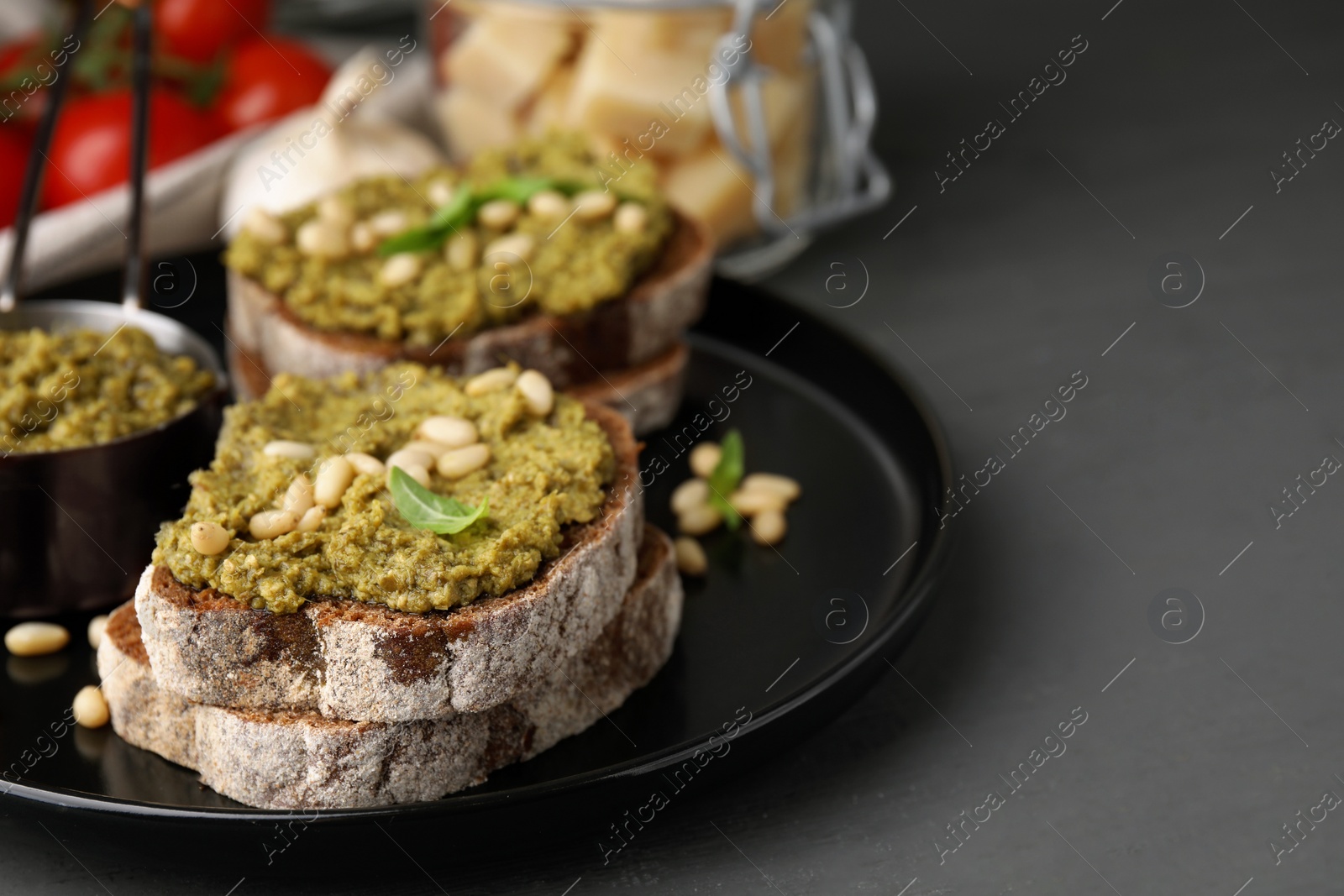 Photo of Tasty bruschettas with pesto sauce and nuts on dark grey table, closeup. Space for text