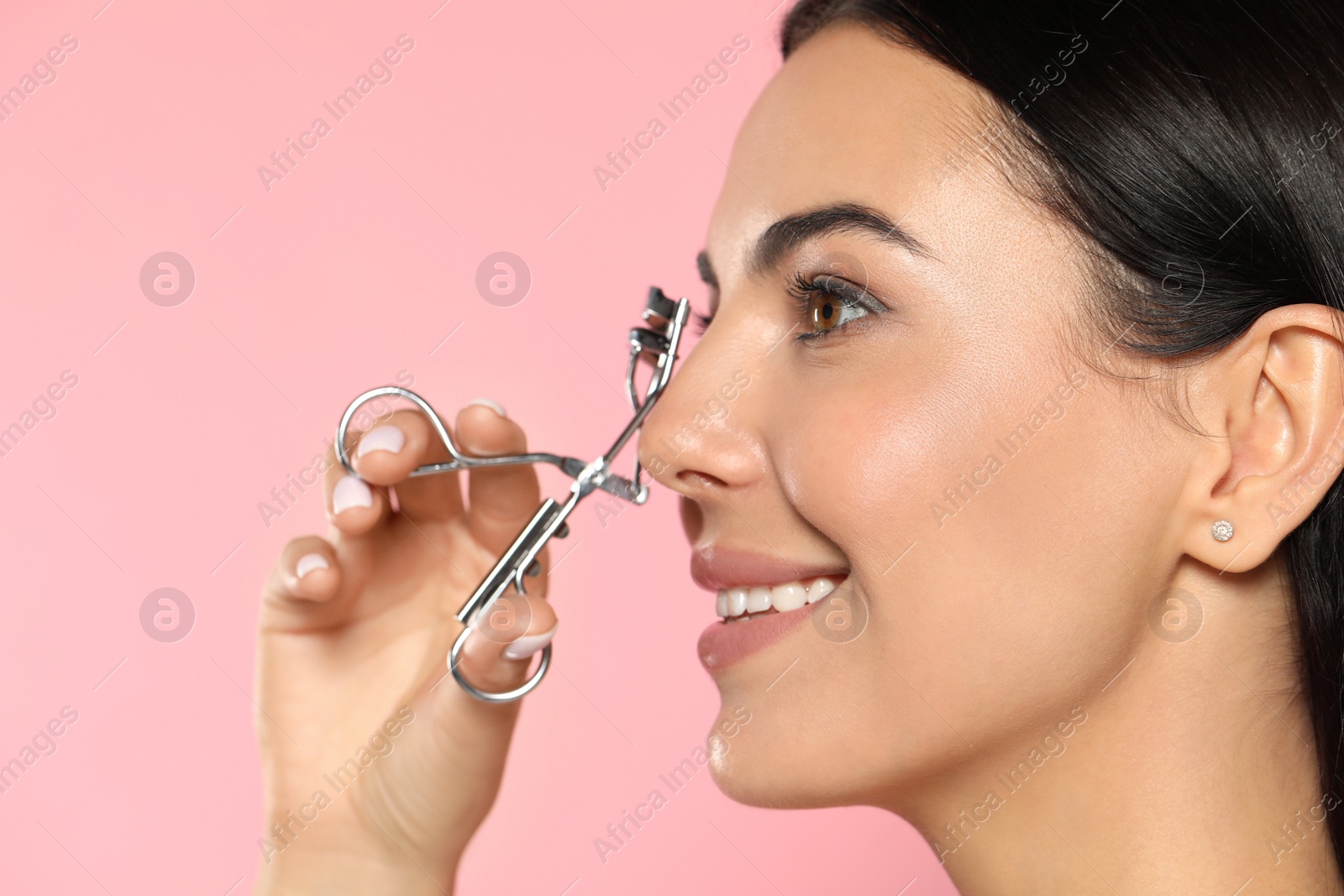 Photo of Beautiful young woman using eyelash curler on light pink background, closeup