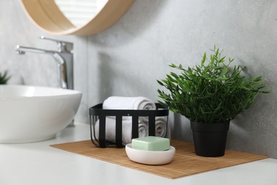 Photo of Potted artificial plant, rolled towels and soap near sink on bathroom vanity