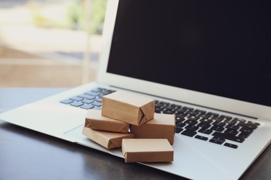 Internet shopping. Modern laptop with small boxes on table indoors, closeup