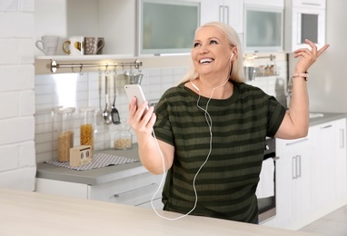 Photo of Mature woman listening to music on mobile phone at home