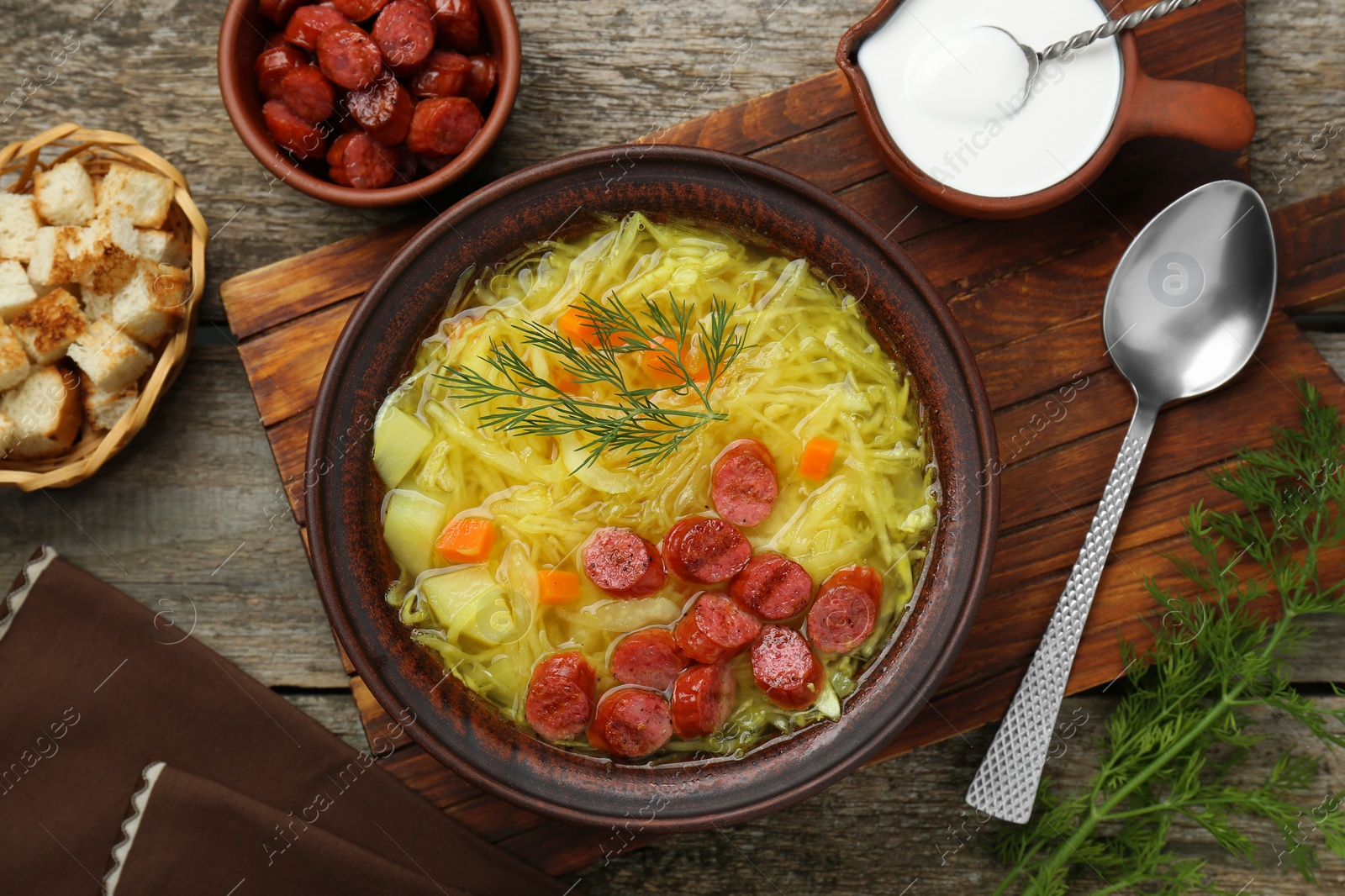 Photo of Delicious sauerkraut soup with smoked sausages and dill served on old wooden table, flat lay