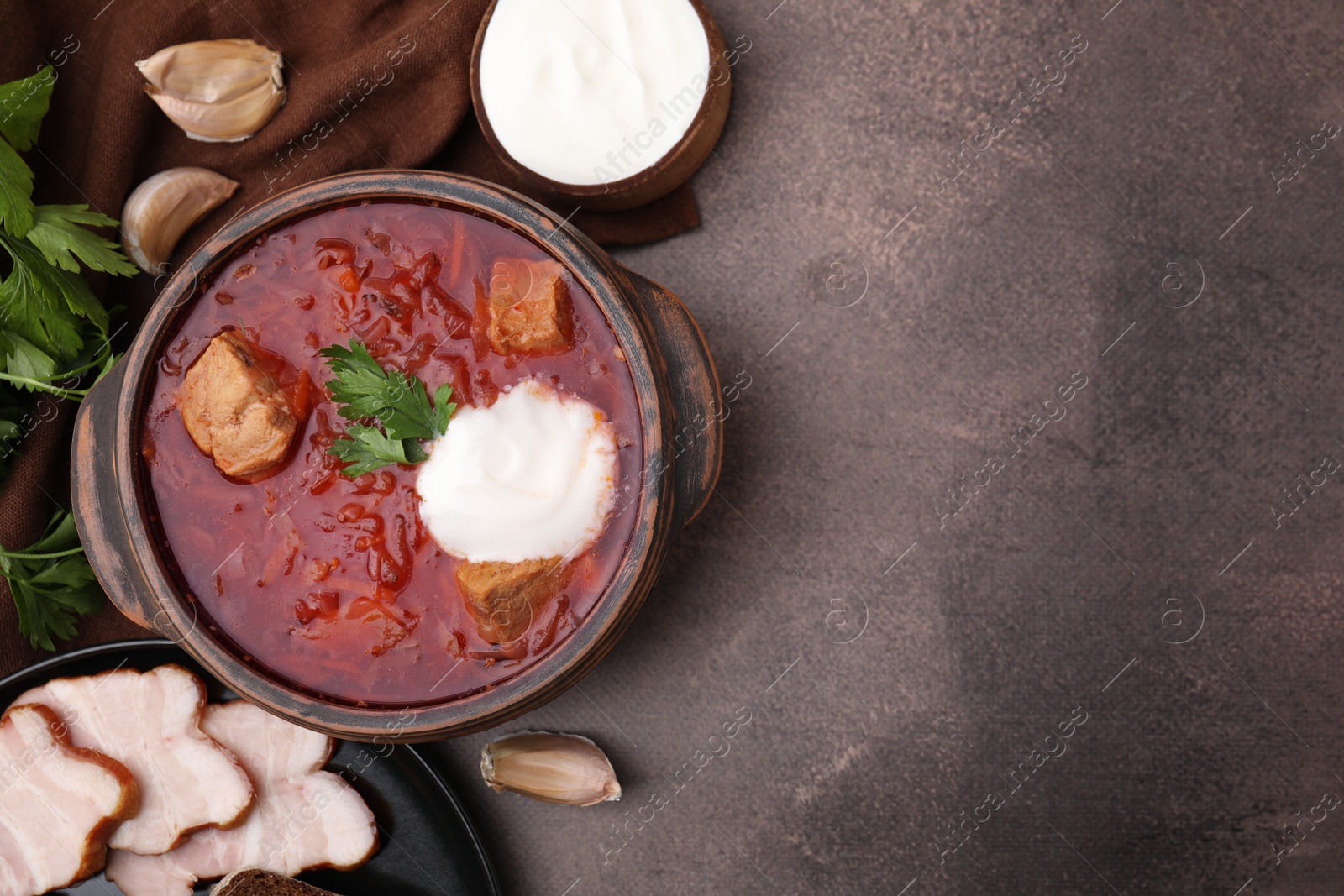 Photo of Tasty borscht with sour cream in bowl served on brown textured table, flat lay. Space for text