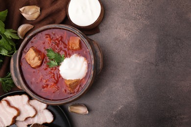 Photo of Tasty borscht with sour cream in bowl served on brown textured table, flat lay. Space for text