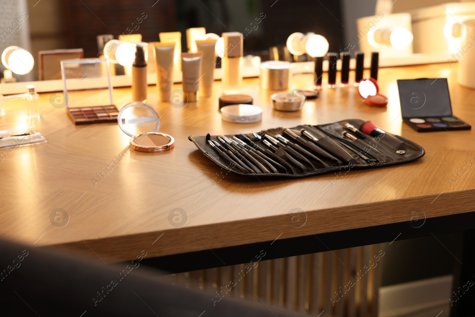 Photo of Set of makeup brushes and cosmetics on wooden table in room