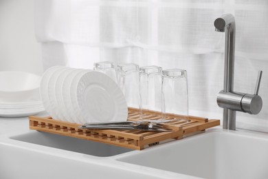 Photo of Drying rack with clean dishes and cutlery on sink in kitchen