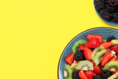 Plate of yummy fruit salad on yellow background, top view. Space for text