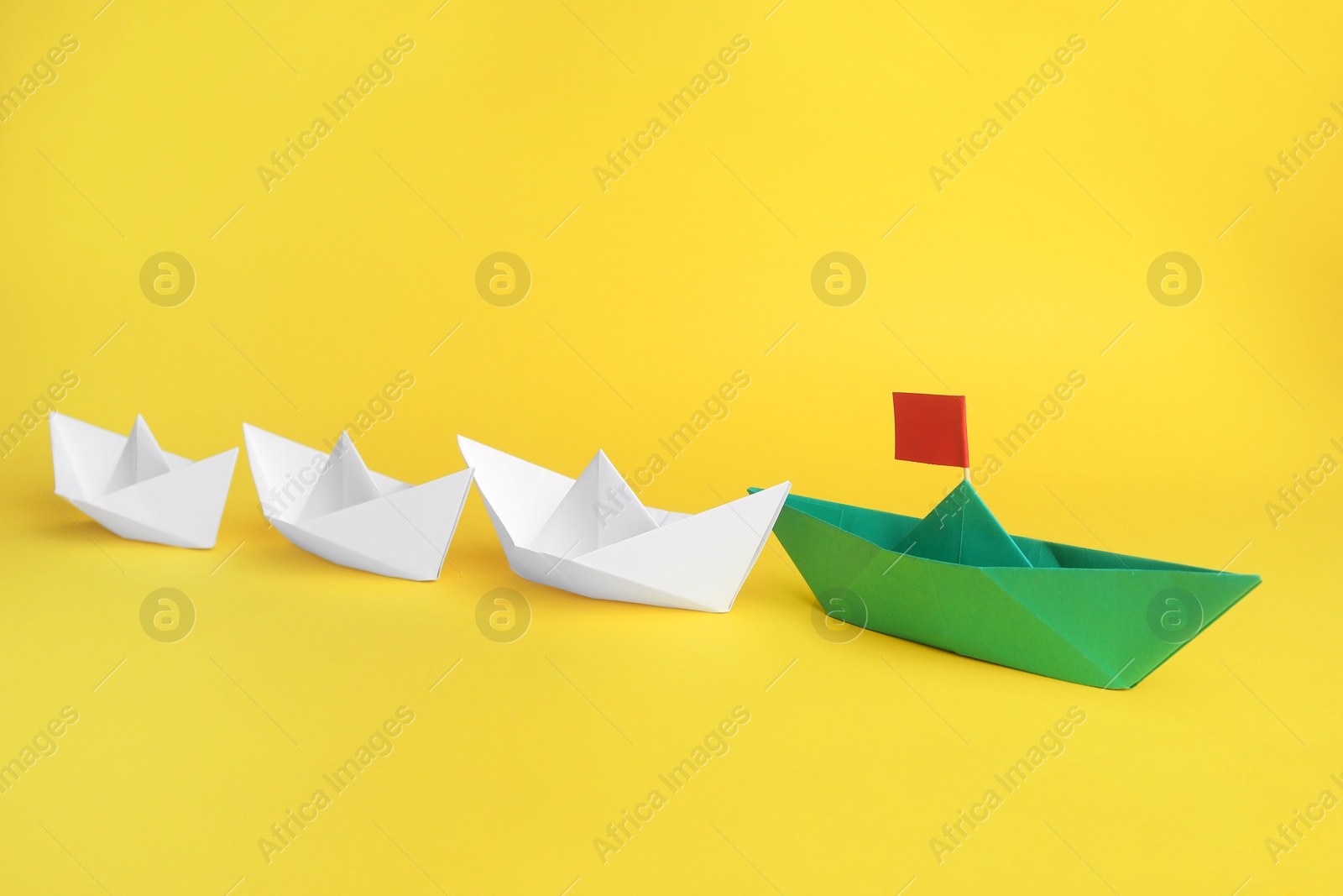 Photo of Group of paper boats following green one on yellow background,. Leadership concept