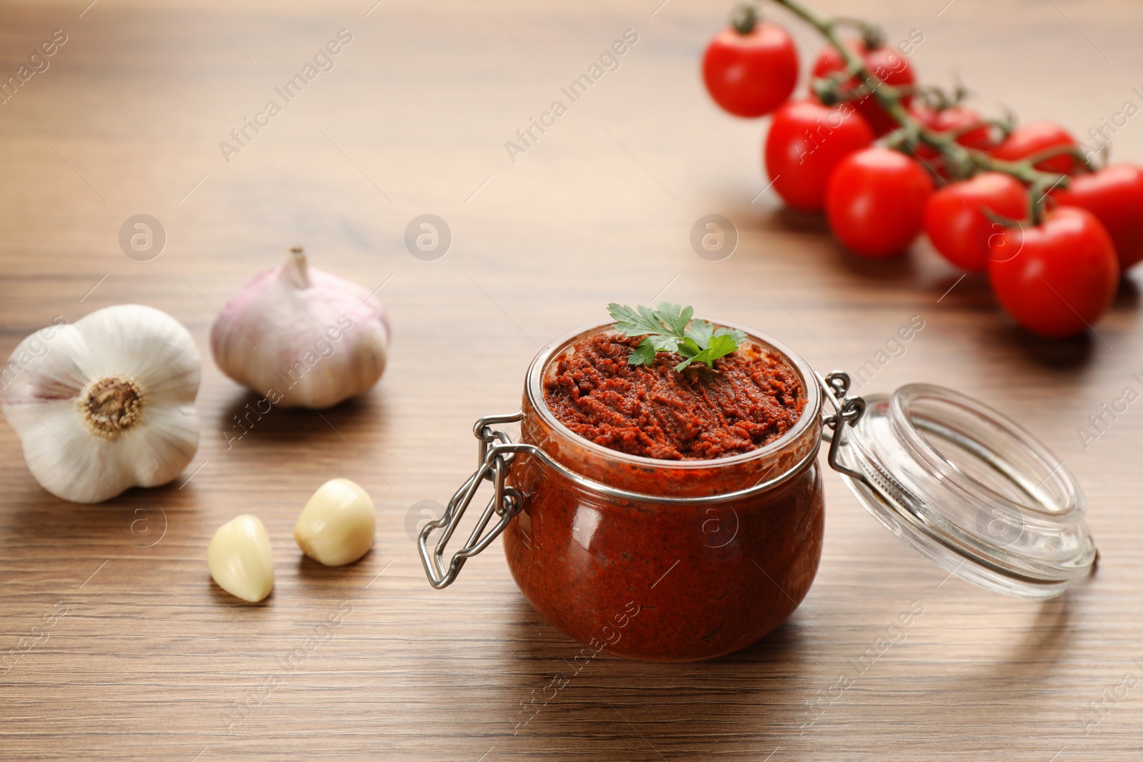 Photo of Delicious adjika sauce in glass jar and ingredients on wooden table