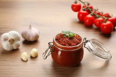 Photo of Delicious adjika sauce in glass jar and ingredients on wooden table