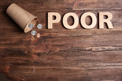 Cup with coins, word POOR and space for text on wooden background, top view