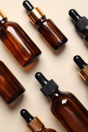 Many bottles with face serums on beige background, flat lay