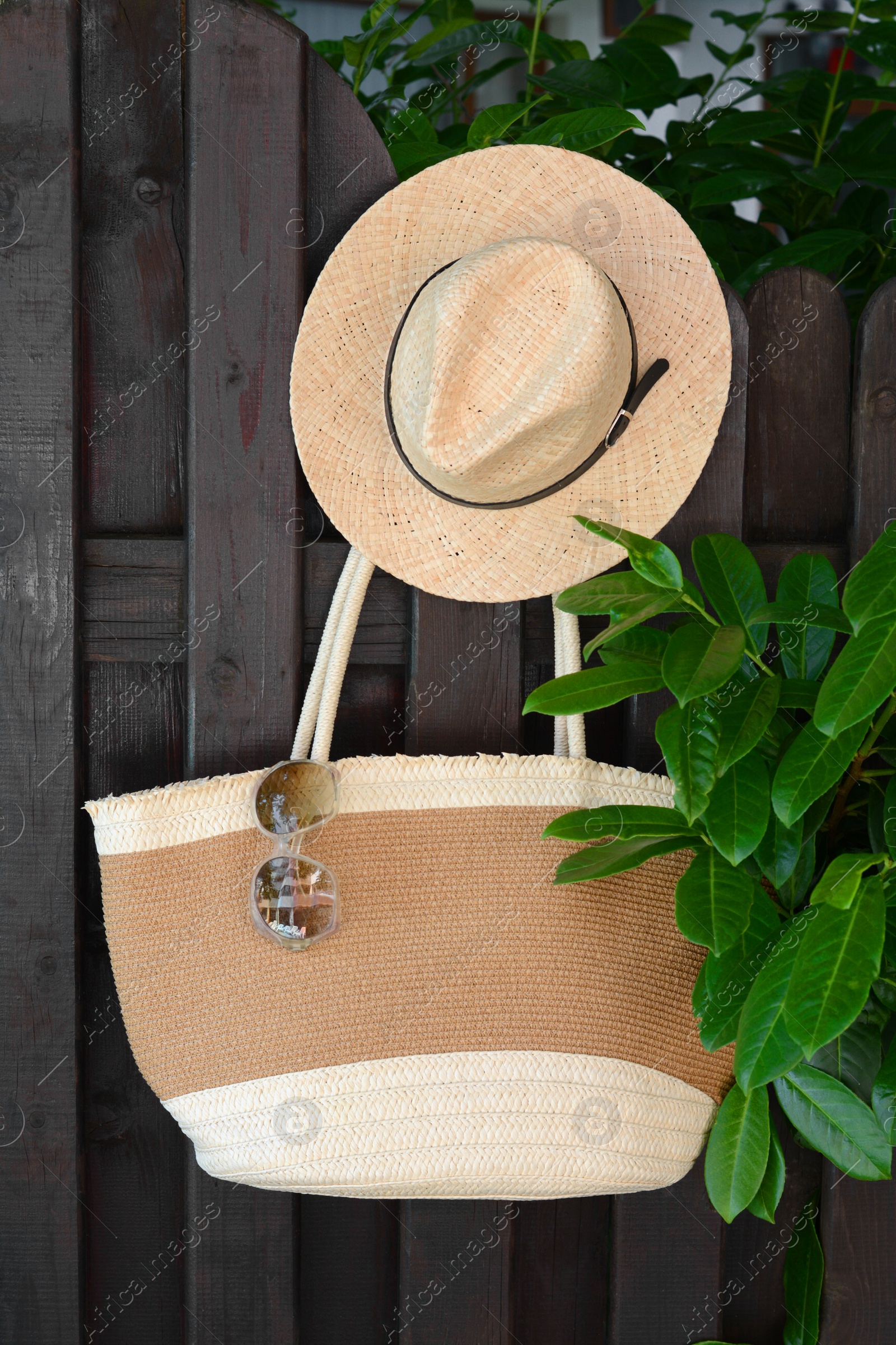Photo of Stylish bag with hat and sunglasses hanging on wooden fence outdoors. Beach accessories