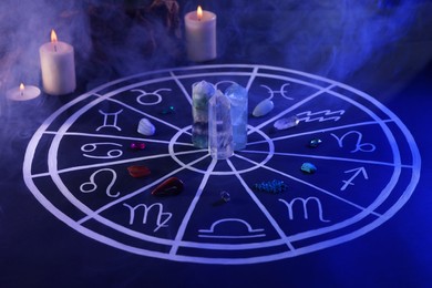 Natural stones for zodiac signs, drawn astrology chart and burning candles on dark blue table