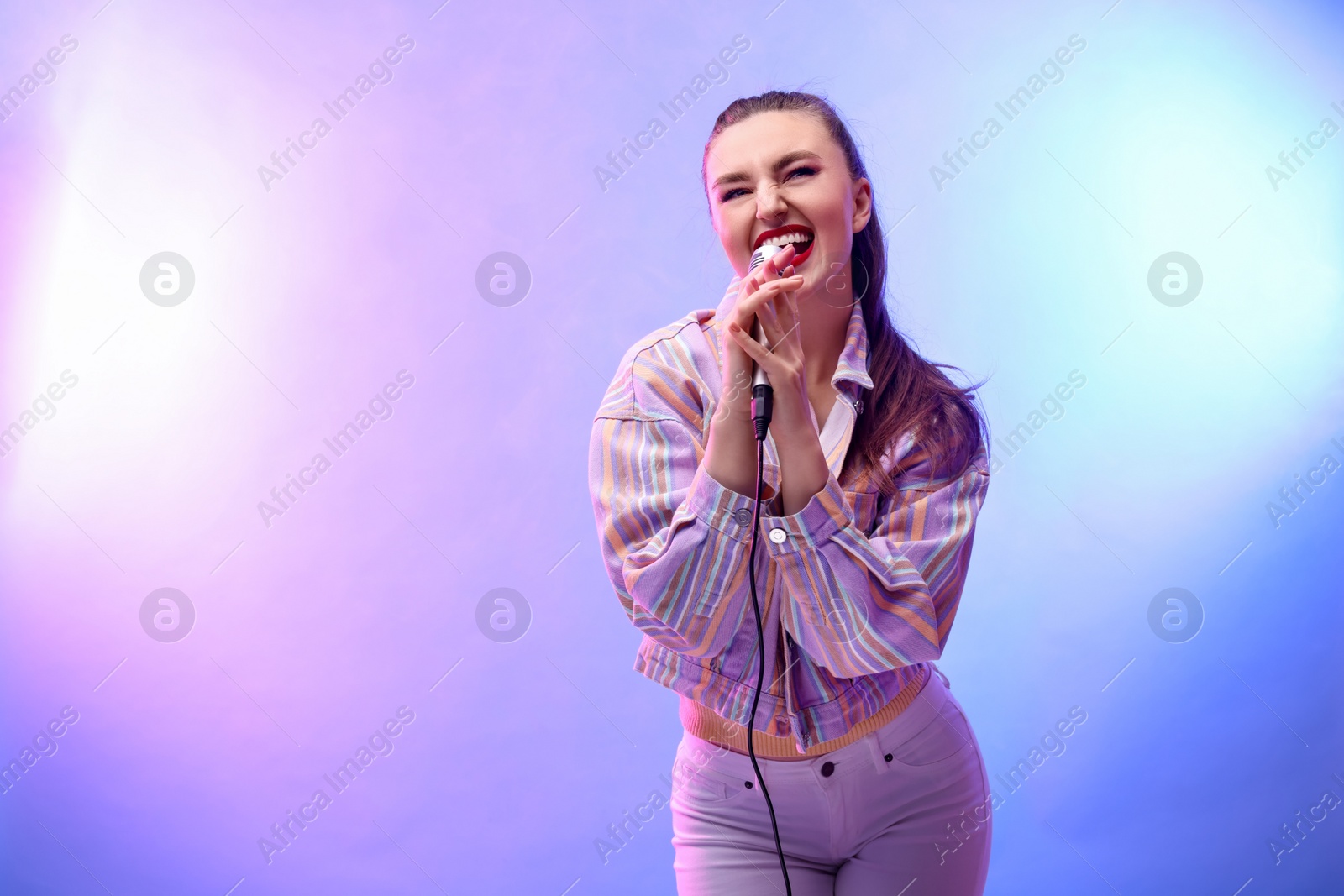 Photo of Emotional woman with microphone singing in color lights. Space for text