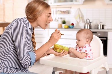 Photo of Woman feeding her child in highchair indoors. Healthy baby food