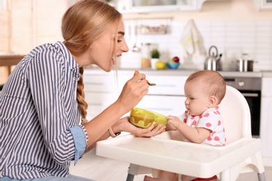 Woman feeding her child in highchair indoors. Healthy baby food