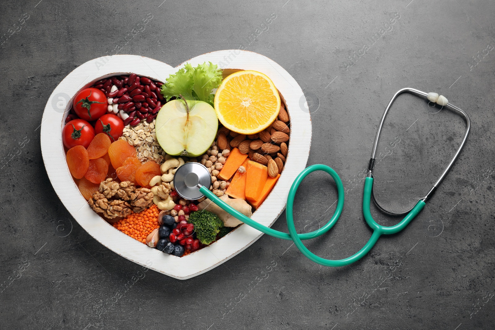 Photo of Heart shaped tray with healthy products and stethoscope on grey background, top view