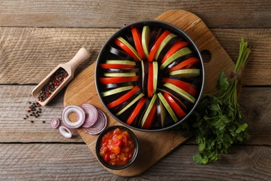 Photo of Cooking delicious ratatouille. Different fresh vegetables, scoop with spices and round baking pan on wooden table, flat lay