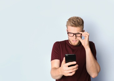Photo of Young man with glasses using mobile phone on light background. Vision problem