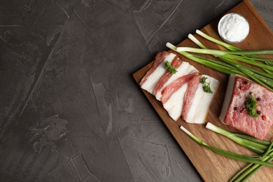 Photo of Board with pork fatback, onions and salt on black stone background, top view. Space for text