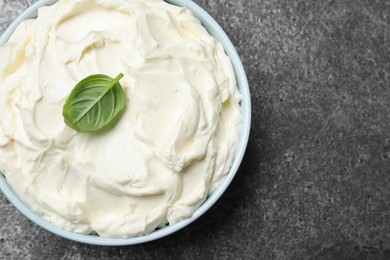 Photo of Bowl of tasty cream cheese and basil leaf on grey table, top view. Space for text