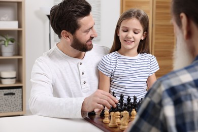 Photo of Family playing chess together at table in room