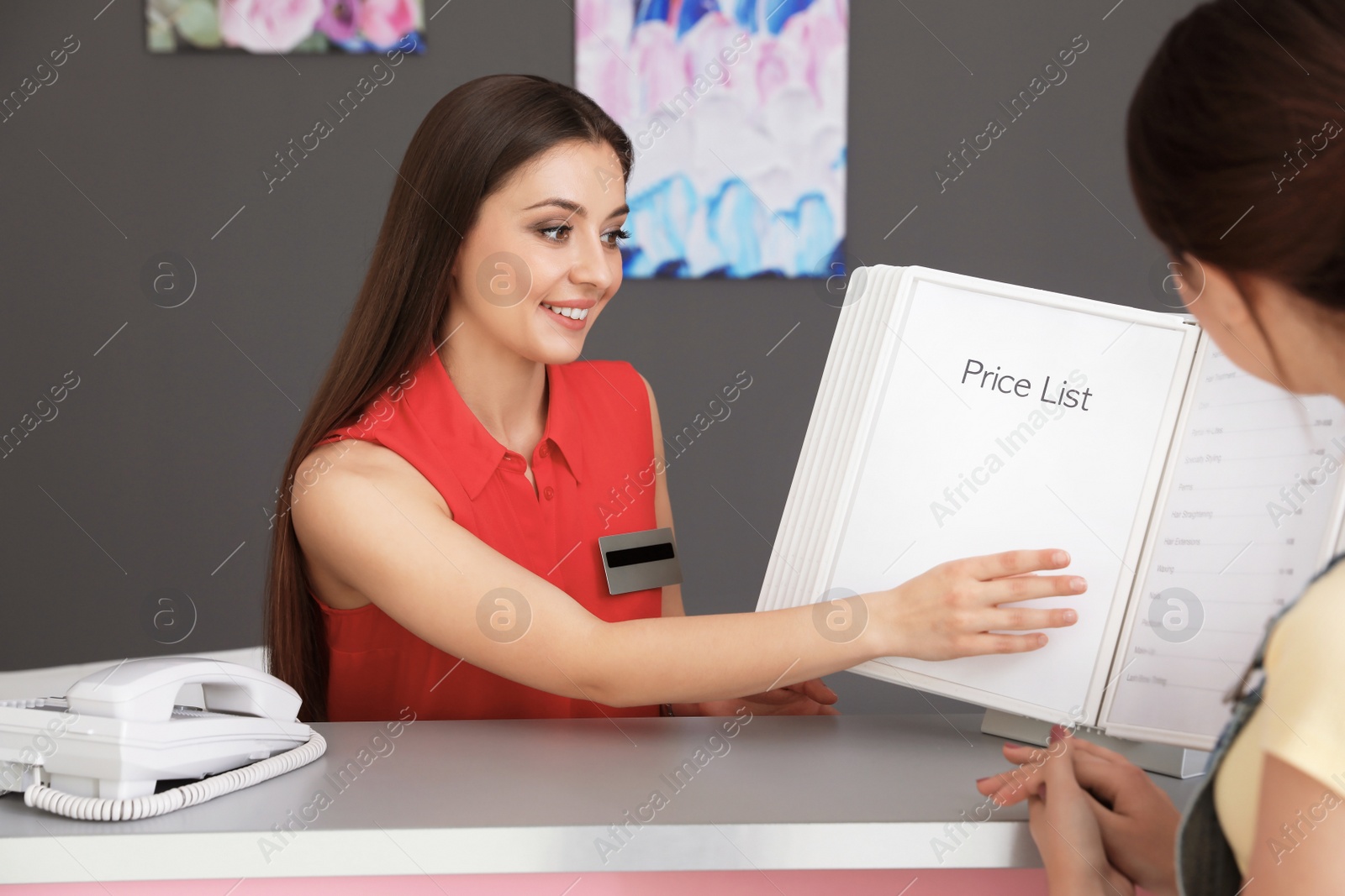 Photo of Young receptionist showing price list to client in beauty salon