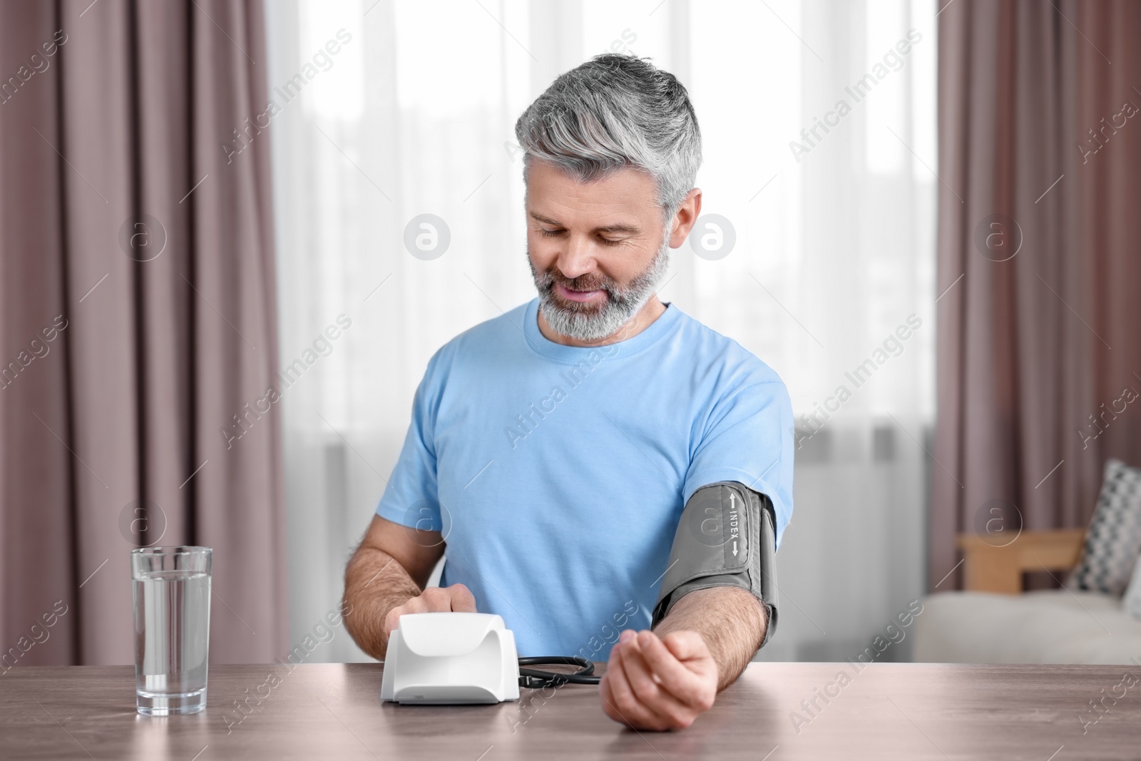 Photo of Man measuring blood pressure at table indoors